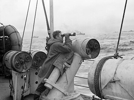 Battle of the Atlantic - A lookout of a convoy escort, posing his binoculars on a depth charge thrower with which depth charges were launched to the sides of the escort. Photo credit: wikipedia