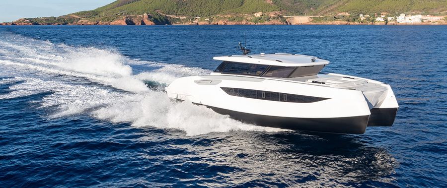 A Sunreef Yachts catamaran powers across the water with a mountainous coastline behind it.