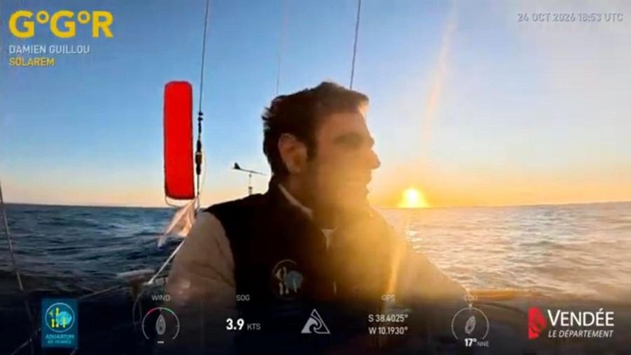 Damien Guillou in profile in the cockpit of Solarem, with the low sun on the horizon, an orange lifebuoy beside him and calm sea behind
