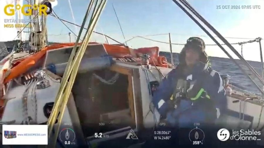 Ertan Beskardes in blue wet-weather gear and a fur-lined hat sitting in the cockpit of Miss Beagle under an orange spray hood, with a blue sea and sky behind.