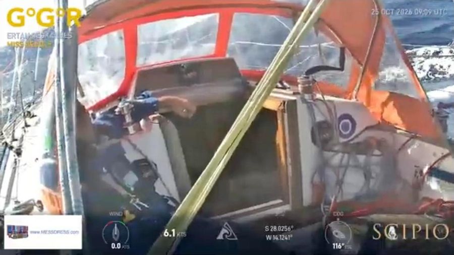 Cockpit of Miss Beagle with an orange spray hood, a sailor in blue gear at the winch and white water streaming past on the right.
