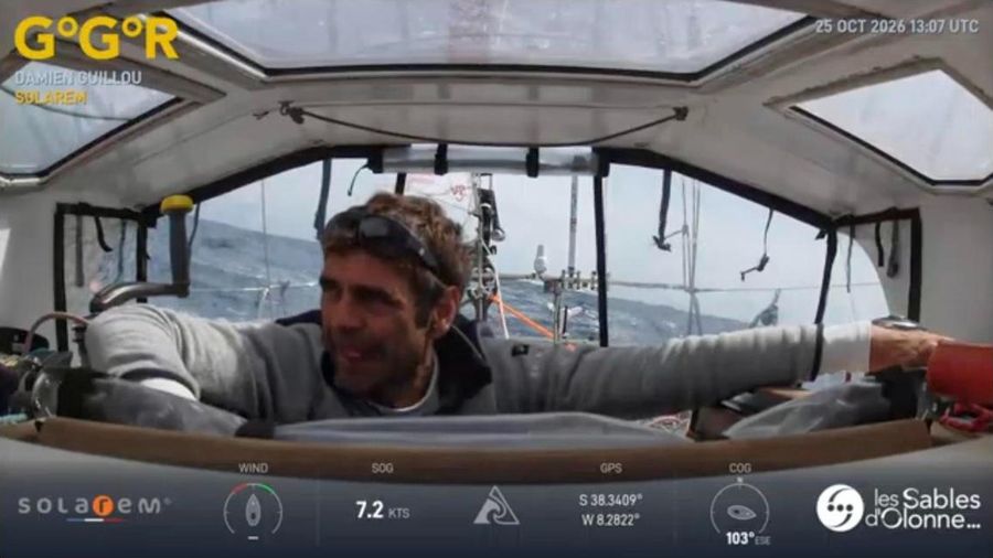Damien Guillou in a grey top with sunglasses pushed up on his head, smiling in the doghouse of Solarem with a rough sea visible through the windows behind him.