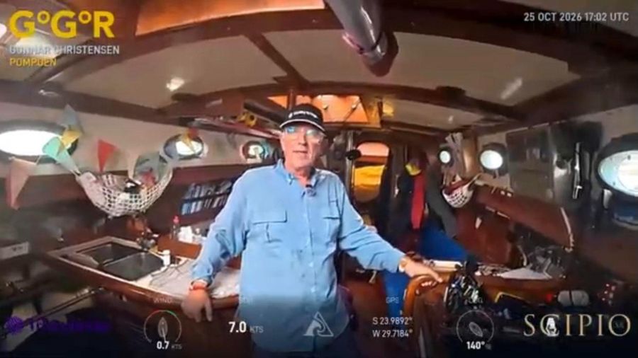 Gunnar Christensen in a pale blue shirt and cap standing in the saloon of Pompoen, with bunting strung from the deckhead and a galley sink behind him.