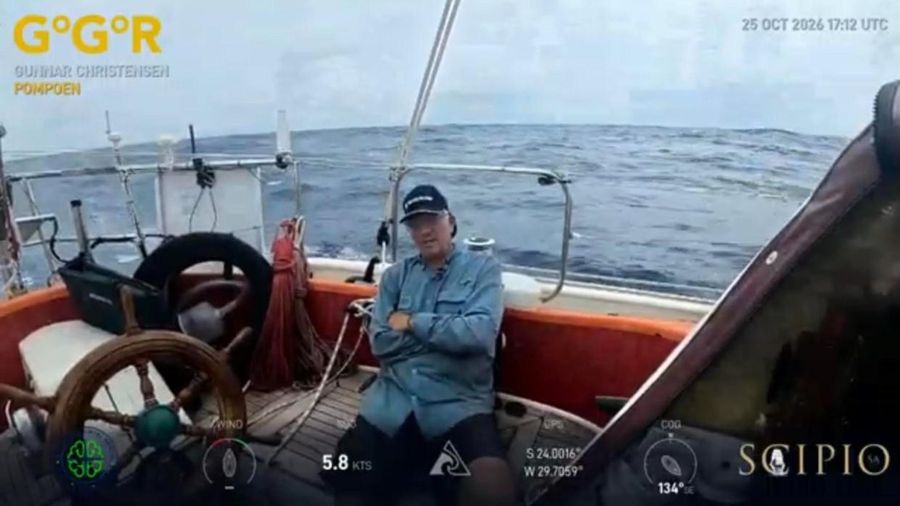 Gunnar Christensen sitting in the cockpit of Pompoen beside the wheel, with a rough blue sea and grey sky behind him.