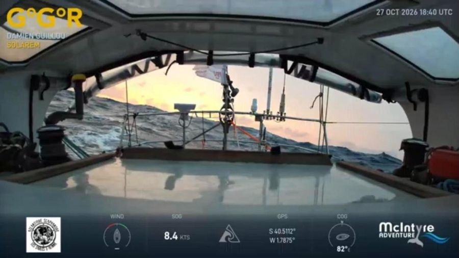 View from inside the cockpit of Solarem at dusk, with a pink sky and a large grey swell breaking beyond the guardrail, the overlay showing 8.4 knots.