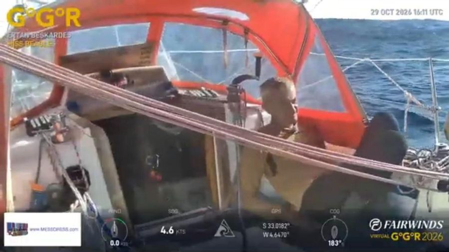 Ertan Beskardes in a yellow top in the cockpit of Miss Beagle under an orange spray hood, with blue sea beyond and lines across the foreground, the overlay showing 4.6 knots at 33 degrees south.