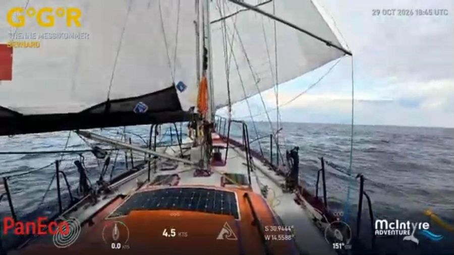 View along the deck of Bernard, with a white sail overhead and an orange solar panel on the cabin top, a grey-blue sea and cloudy sky beyond, the overlay showing 4.5 knots at 31 degrees south.