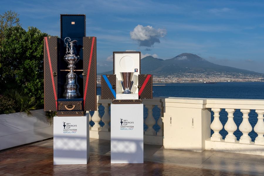 The America's Cup and Louis Vuitton trophies on display in Naples, with Mount Vesuvius visible in the background.